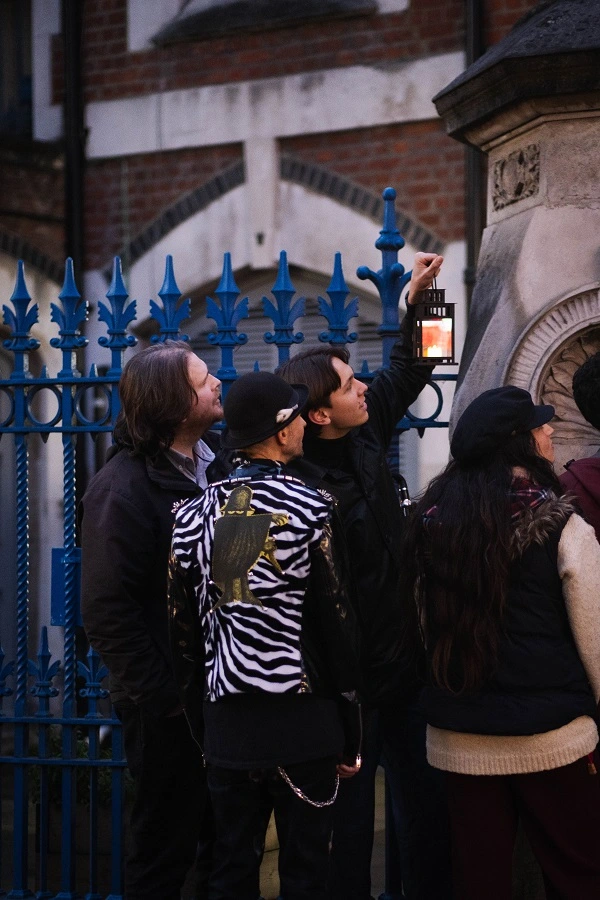 Jack the Ripper tour guide holding a lantern and pointing out a historic Whitechapel landmark to a group of tourists at night