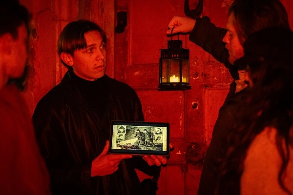 Jack the Ripper tour guide showing a historic illustration by lantern light during the immersive storytelling experience